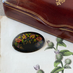 Vintage Russian hand‑painted floral black lacquer oval brooch with red, pink, and yellow flowers and gold detailing.