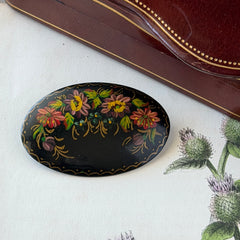 Vintage Russian hand‑painted floral black lacquer oval brooch with red, pink, and yellow flowers and gold detailing.