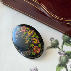 Vintage Russian hand‑painted floral black lacquer oval brooch with red, pink, and yellow flowers and gold detailing.