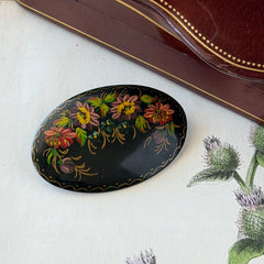 Vintage Russian hand‑painted floral black lacquer oval brooch with red, pink, and yellow flowers and gold detailing.