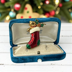 Vintage SFJ Christmas stocking brooch in gold tone metal with red, green, and white enamel; features teddy bear and holly details, signed SFJ on back.