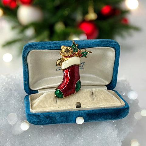 Vintage SFJ Christmas stocking brooch in gold tone metal with red, green, and white enamel; features teddy bear and holly details, signed SFJ on back.