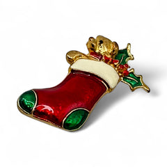 Vintage SFJ Christmas stocking brooch in gold tone metal with red, green, and white enamel; features teddy bear and holly details, signed SFJ on back.