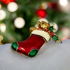 Vintage SFJ Christmas stocking brooch in gold tone metal with red, green, and white enamel; features teddy bear and holly details, signed SFJ on back.