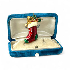 Vintage SFJ Christmas stocking brooch in gold tone metal with red, green, and white enamel; features teddy bear and holly details, signed SFJ on back.