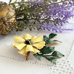 Vintage Sandor yellow enamel flower brooch with green leaves and gold tone accents.