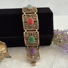 Ornate gold‑tone Sarah Coventry Granada panel bracelet with five colorful oval faux cabochons.