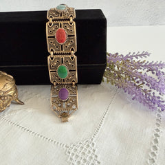 Ornate gold‑tone Sarah Coventry Granada panel bracelet with five colorful oval faux cabochons.