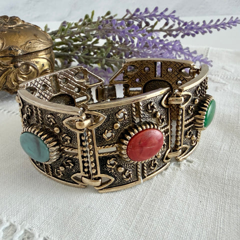 Ornate gold‑tone Sarah Coventry Granada panel bracelet with five colorful oval faux cabochons.