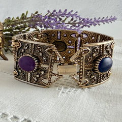 Ornate gold‑tone Sarah Coventry Granada panel bracelet with five colorful oval faux cabochons.