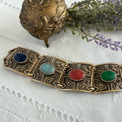 Ornate gold‑tone Sarah Coventry Granada panel bracelet with five colorful oval faux cabochons.