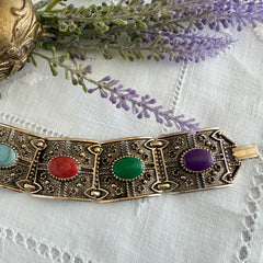 Ornate gold‑tone Sarah Coventry Granada panel bracelet with five colorful oval faux cabochons.