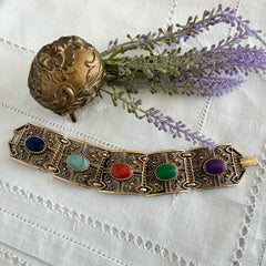 Ornate gold‑tone Sarah Coventry Granada panel bracelet with five colorful oval faux cabochons.