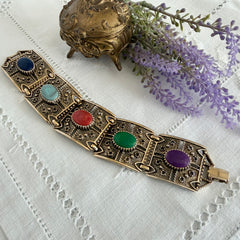 Ornate gold‑tone Sarah Coventry Granada panel bracelet with five colorful oval faux cabochons.