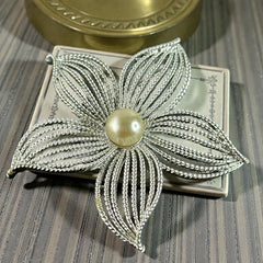 Vintage 1967 Sarah Coventry ‘Moon Flower’ brooch with silver‑tone openwork petals and a central faux pearl, shown in close detail to highlight its sculptural mid‑century design.