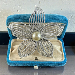 Vintage 1967 Sarah Coventry ‘Moon Flower’ brooch with silver‑tone openwork petals and a central faux pearl, shown in close detail to highlight its sculptural mid‑century design.
