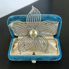 Vintage 1967 Sarah Coventry ‘Moon Flower’ brooch with silver‑tone openwork petals and a central faux pearl, shown in close detail to highlight its sculptural mid‑century design.