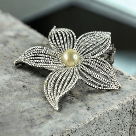 Vintage 1967 Sarah Coventry ‘Moon Flower’ brooch with silver‑tone openwork petals and a central faux pearl, shown in close detail to highlight its sculptural mid‑century design.