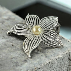 Vintage 1967 Sarah Coventry ‘Moon Flower’ brooch with silver‑tone openwork petals and a central faux pearl, shown in close detail to highlight its sculptural mid‑century design.