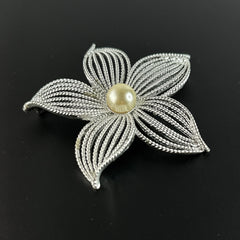 Vintage 1967 Sarah Coventry ‘Moon Flower’ brooch with silver‑tone openwork petals and a central faux pearl, shown in close detail to highlight its sculptural mid‑century design.