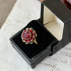 Vintage gold‑tone Sarah Coventry ring with red rhinestones in a raised floral cluster design, adjustable band, signed Sarah Cov.
