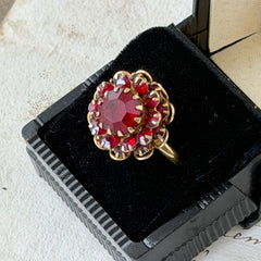 Vintage gold‑tone Sarah Coventry ring with red rhinestones in a raised floral cluster design, adjustable band, signed Sarah Cov.