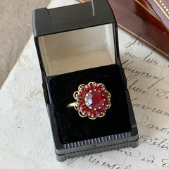 Vintage gold‑tone Sarah Coventry ring with red rhinestones in a raised floral cluster design, adjustable band, signed Sarah Cov.