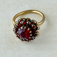 Vintage gold‑tone Sarah Coventry ring with red rhinestones in a raised floral cluster design, adjustable band, signed Sarah Cov.
