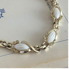 Vintage Sarah Coventry necklace with white ribbed thermoset panels, clear rhinestones, and gold‑tone links, shown from multiple angles to display its mid‑century design.