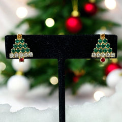 Pair of vintage Sarah Coventry clip-on earrings shaped like Christmas trees, featuring clear and green rhinestones as leaves, a red rhinestone trunk, and a yellow rhinestone star at the top. Gold tone metal with signed clips. Small size, festive design.