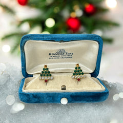 Pair of vintage Sarah Coventry clip-on earrings shaped like Christmas trees, featuring clear and green rhinestones as leaves, a red rhinestone trunk, and a yellow rhinestone star at the top. Gold tone metal with signed clips. Small size, festive design.