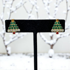 Pair of vintage Sarah Coventry clip-on earrings shaped like Christmas trees, featuring clear and green rhinestones as leaves, a red rhinestone trunk, and a yellow rhinestone star at the top. Gold tone metal with signed clips. Small size, festive design.