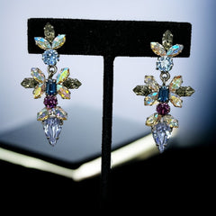 Vintage Schoffel Austria dangle earrings featuring blue, purple, and aurora borealis crystals in silver-tone settings, with floral and teardrop motifs, shown from multiple angles to highlight sparkle, craftsmanship, and signed crown mark.