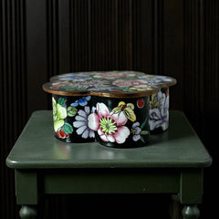 Vintage Seymour Mann flower-shaped trinket box with black enamel exterior, decorated with multicolored floral designs outlined in gold; features a light blue enamel interior and sculpted petal edges.