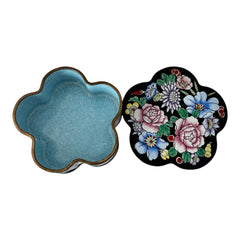 Vintage Seymour Mann flower-shaped trinket box with black enamel exterior, decorated with multicolored floral designs outlined in gold; features a light blue enamel interior and sculpted petal edges.