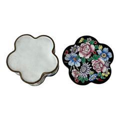 Vintage Seymour Mann flower-shaped trinket box with black enamel exterior, decorated with multicolored floral designs outlined in gold; features a light blue enamel interior and sculpted petal edges.