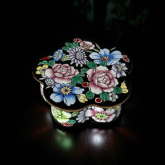 Vintage Seymour Mann flower-shaped trinket box with black enamel exterior, decorated with multicolored floral designs outlined in gold; features a light blue enamel interior and sculpted petal edges.