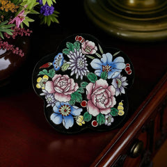 Vintage Seymour Mann flower-shaped trinket box with black enamel exterior, decorated with multicolored floral designs outlined in gold; features a light blue enamel interior and sculpted petal edges.