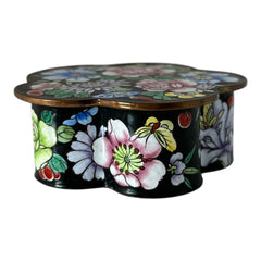 Vintage Seymour Mann flower-shaped trinket box with black enamel exterior, decorated with multicolored floral designs outlined in gold; features a light blue enamel interior and sculpted petal edges.
