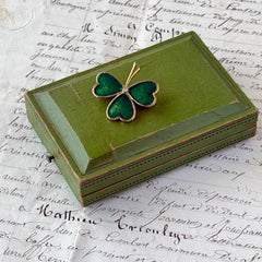 Vintage BJ green enamel shamrock brooch in gold tone with clear rhinestone center, shown in box and on antique French paper.