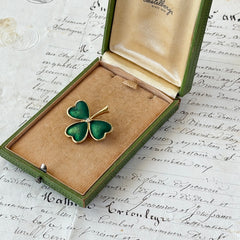 Vintage BJ green enamel shamrock brooch in gold tone with clear rhinestone center, shown in box and on antique French paper.