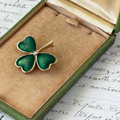 Vintage BJ green enamel shamrock brooch in gold tone with clear rhinestone center, shown in box and on antique French paper.