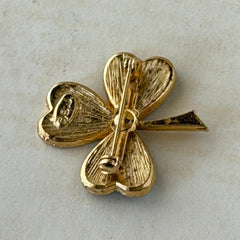 Vintage BJ green enamel shamrock brooch in gold tone with clear rhinestone center, shown in box and on antique French paper.