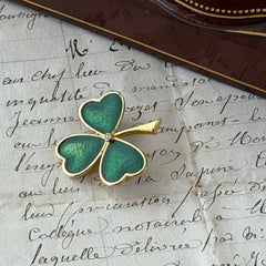 Vintage BJ green enamel shamrock brooch in gold tone with clear rhinestone center, shown in box and on antique French paper.
