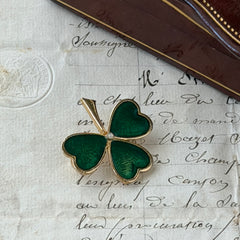 Vintage BJ green enamel shamrock brooch in gold tone with clear rhinestone center, shown in box and on antique French paper.