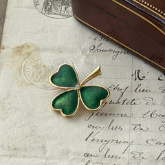 Vintage BJ green enamel shamrock brooch in gold tone with clear rhinestone center, shown in box and on antique French paper.