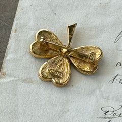 Vintage BJ green enamel shamrock brooch in gold tone with clear rhinestone center, shown in box and on antique French paper.
