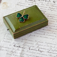 Vintage BJ green enamel shamrock brooch in gold tone with clear rhinestone center, shown in box and on antique French paper.