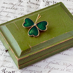 Vintage BJ green enamel shamrock brooch in gold tone with clear rhinestone center, shown in box and on antique French paper.