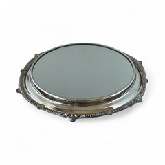 Vintage Sheffield Silver Co. Shrewsbury Plateau round silver-plated tray with mirrored surface and ornate floral scrollwork border; footed design with four decorative legs; shown outdoors with sky and leaves reflected in mirror; very good vintage condition with original packaging and maker’s sticker from Norton, Massachusetts.